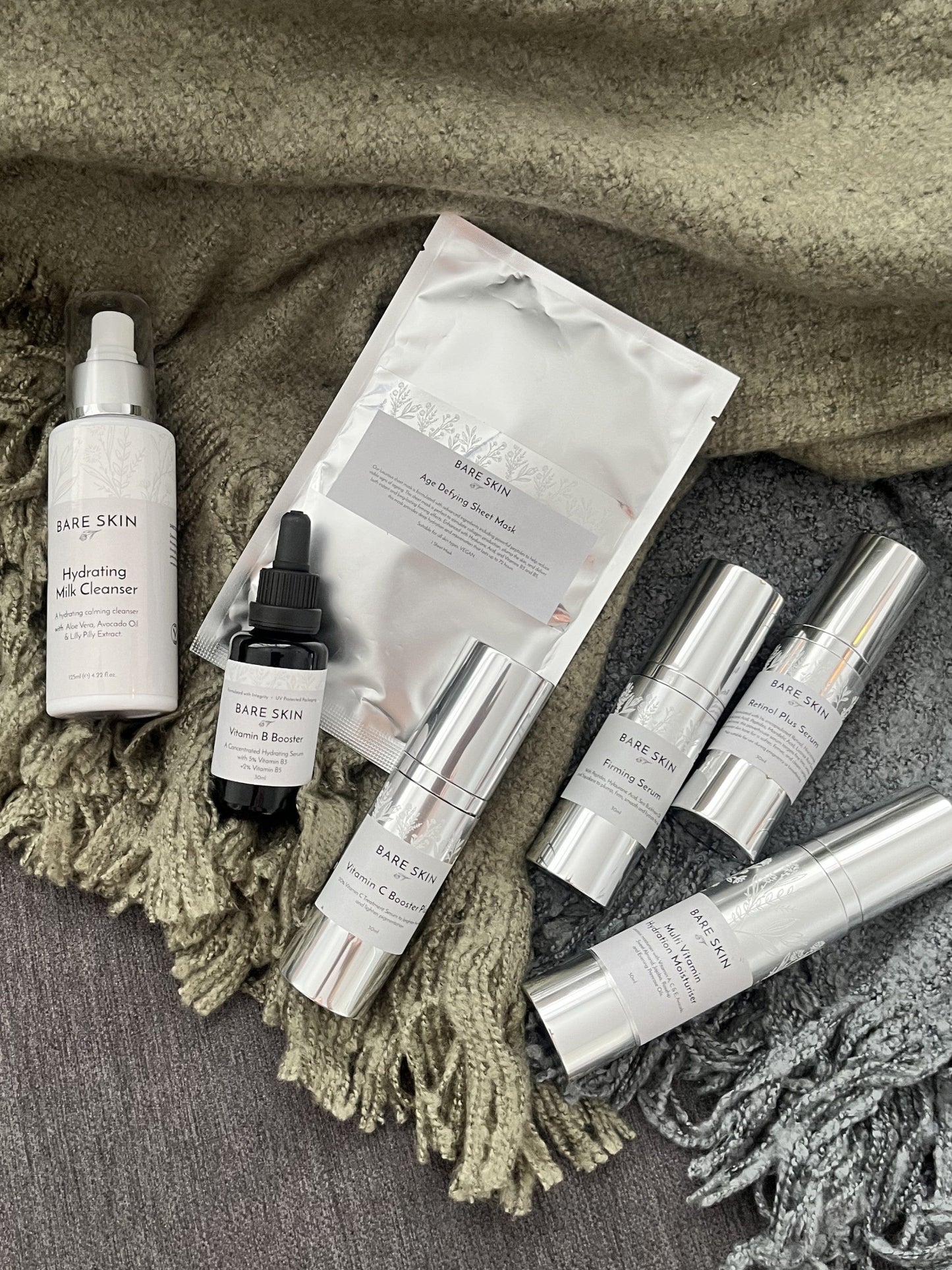 Bare Skin Ageless Glow Skincare Kit products on textured fabric with green and grey blankets, anti-aging hydrating and firming skincare.