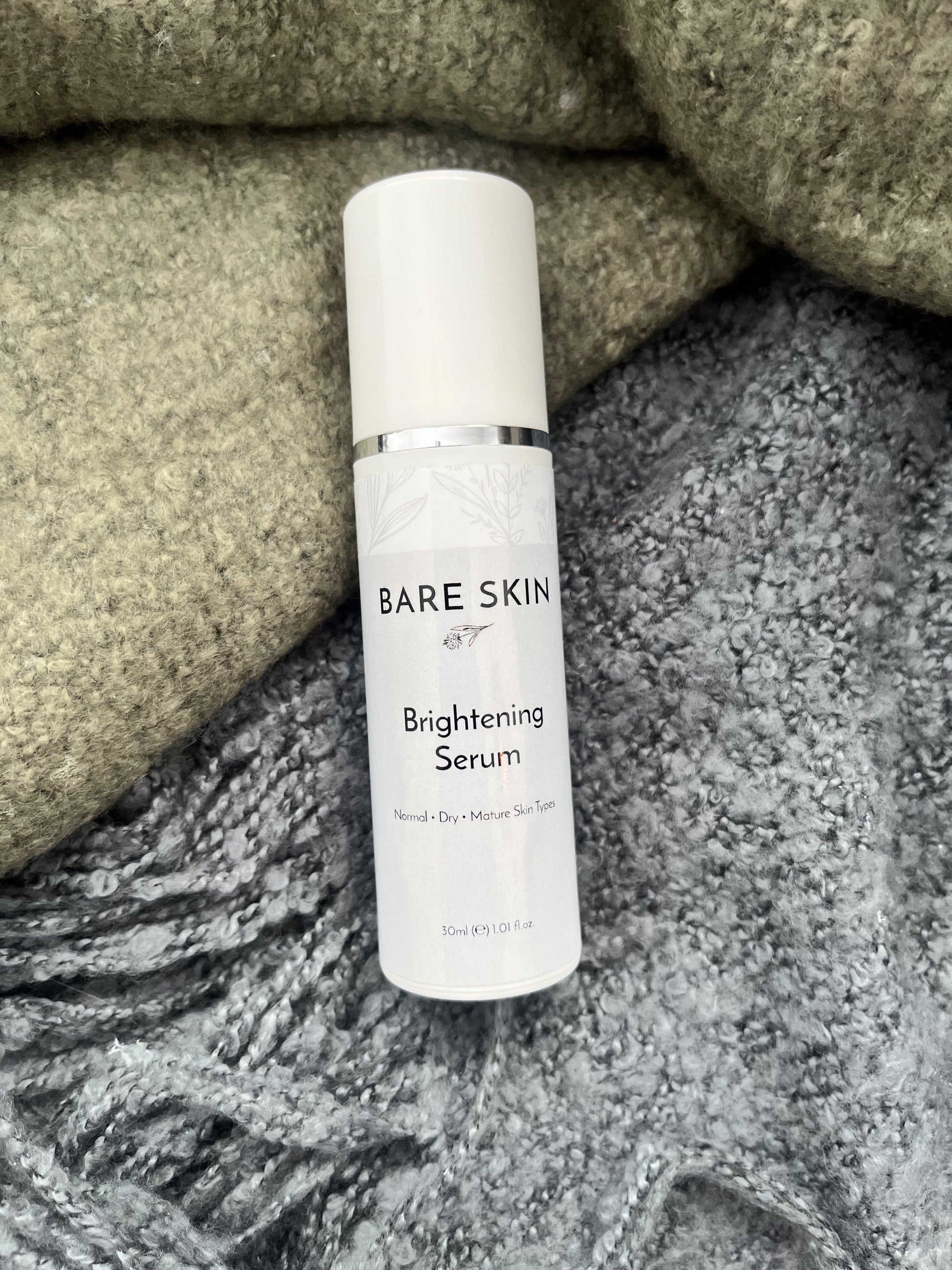 Bare Skin Brightening Serum bottle resting on a green and grey blanket, skincare for radiant glowing skin.