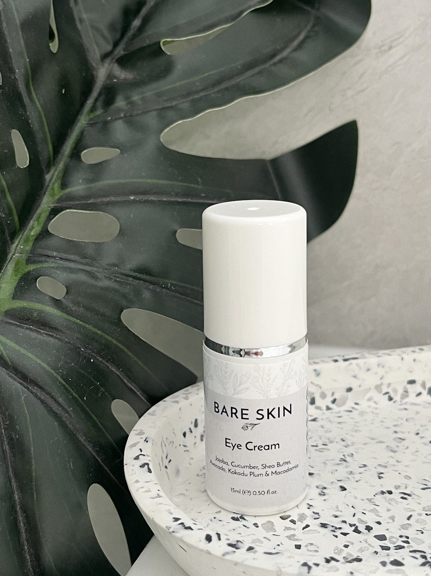 Bare Skin Hydrating Eye Cream with Cucumber, Kakadu Plum and Jojoba bottle on speckled ceramic tray with leafy background, hydrating nourishing eye care.