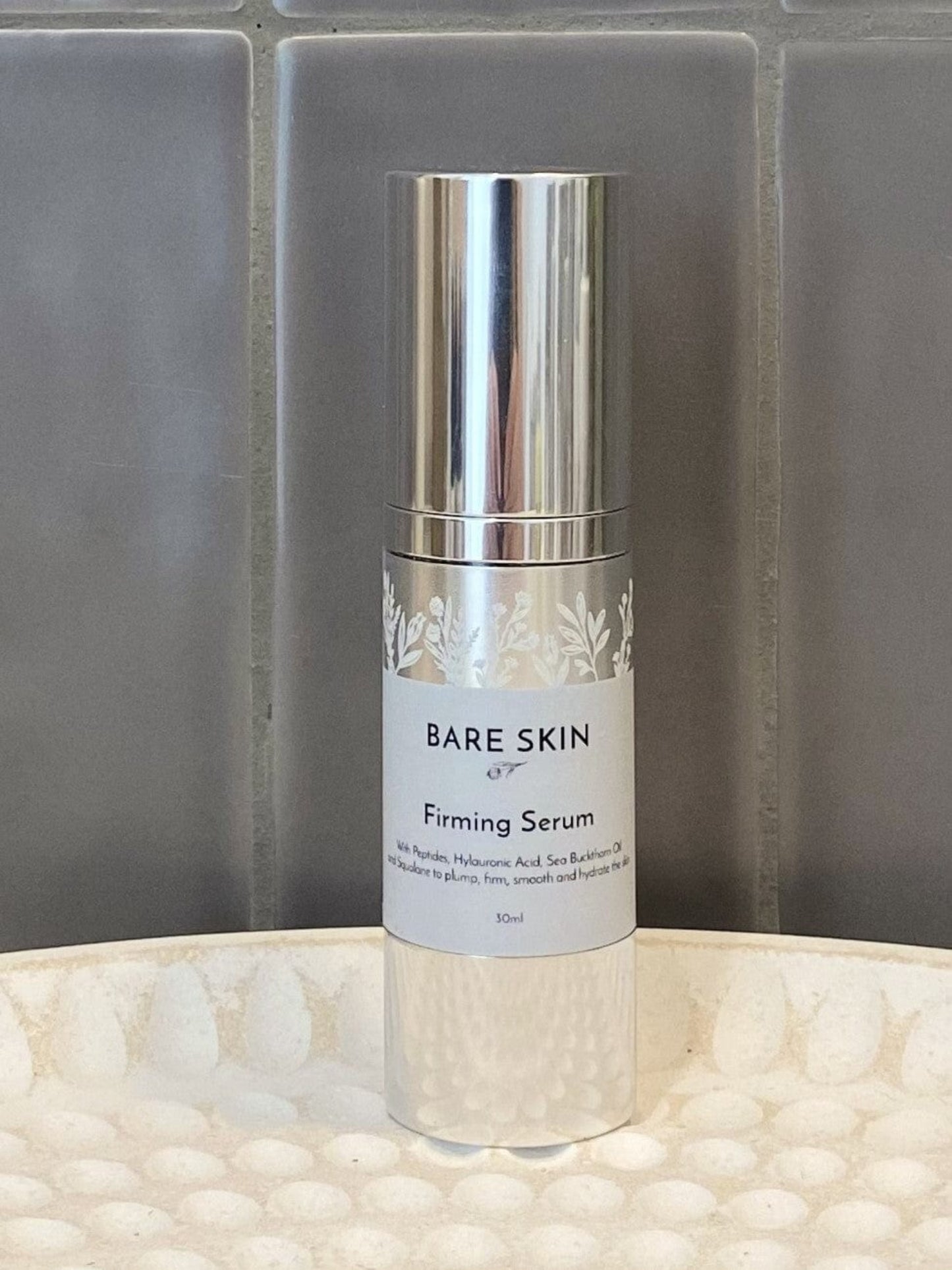 Bare Skin Firming Serum bottle on a textured surface with a gray tiled background