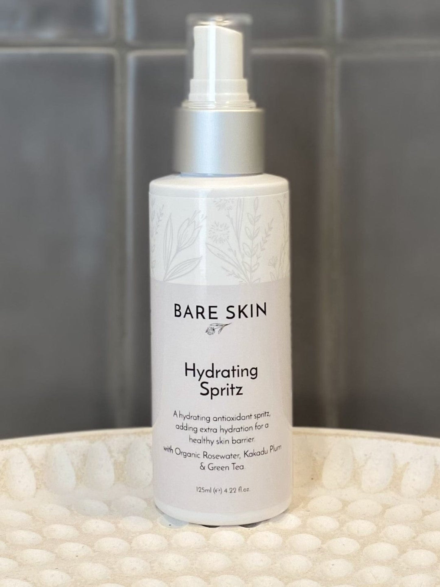 Bare Skin Hydrating Spritz bottle on a textured surface with tiled wall background