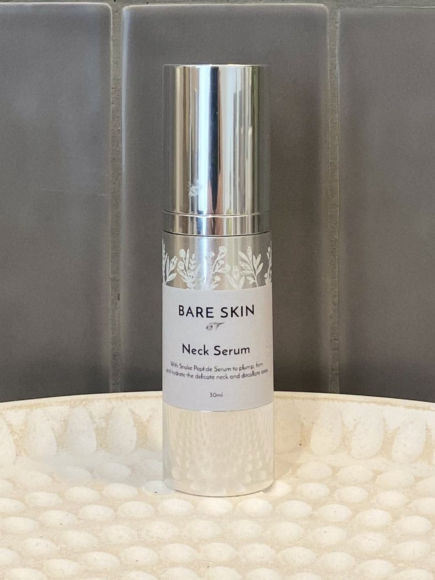 Bare Skin Neck Serum bottle on a textured surface with a gray tiled background