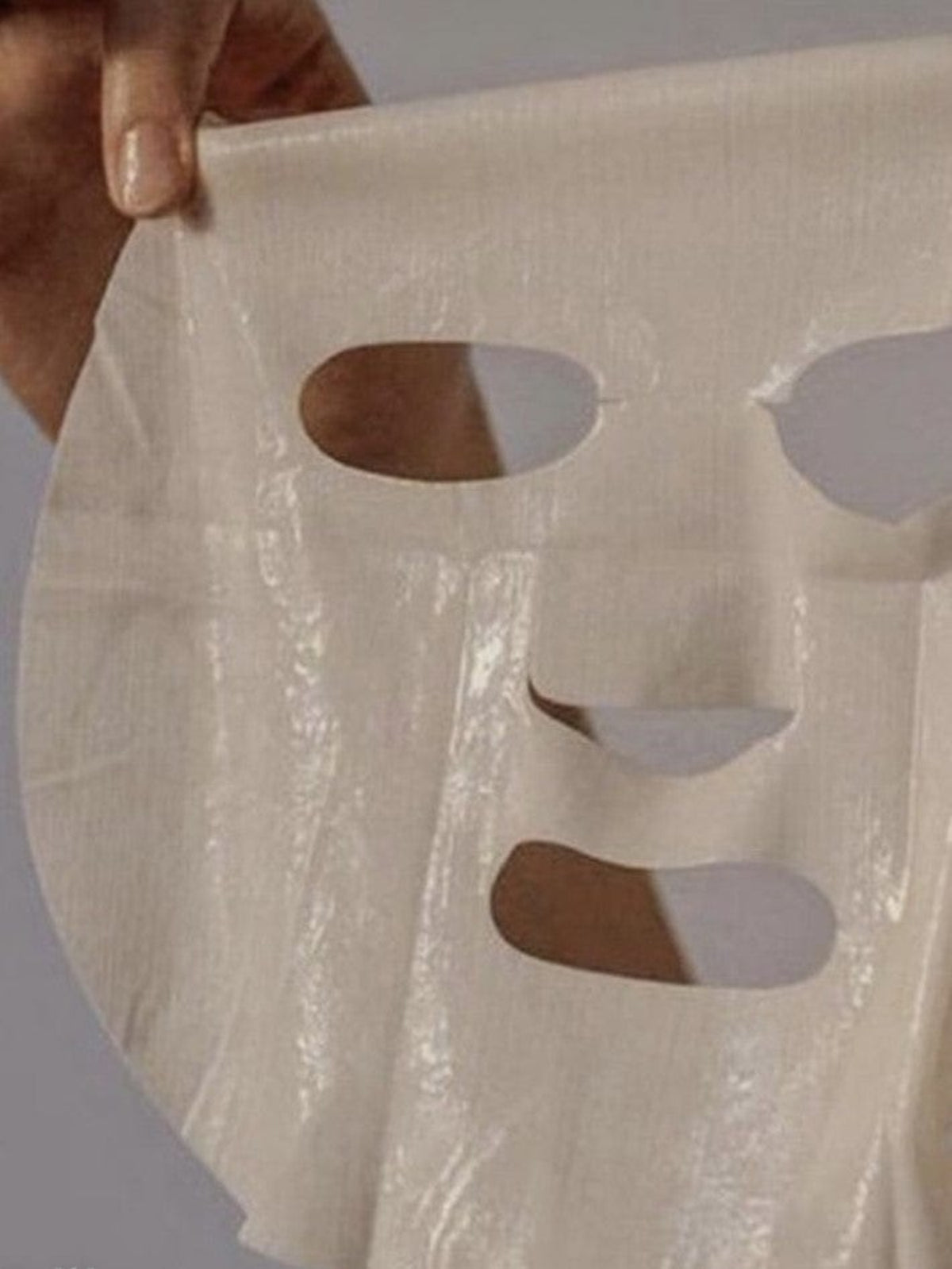 Bare Skin Age Defying Sheet Mask held up by hand with fingers visible, hydrating firming and anti-aging face treatment.