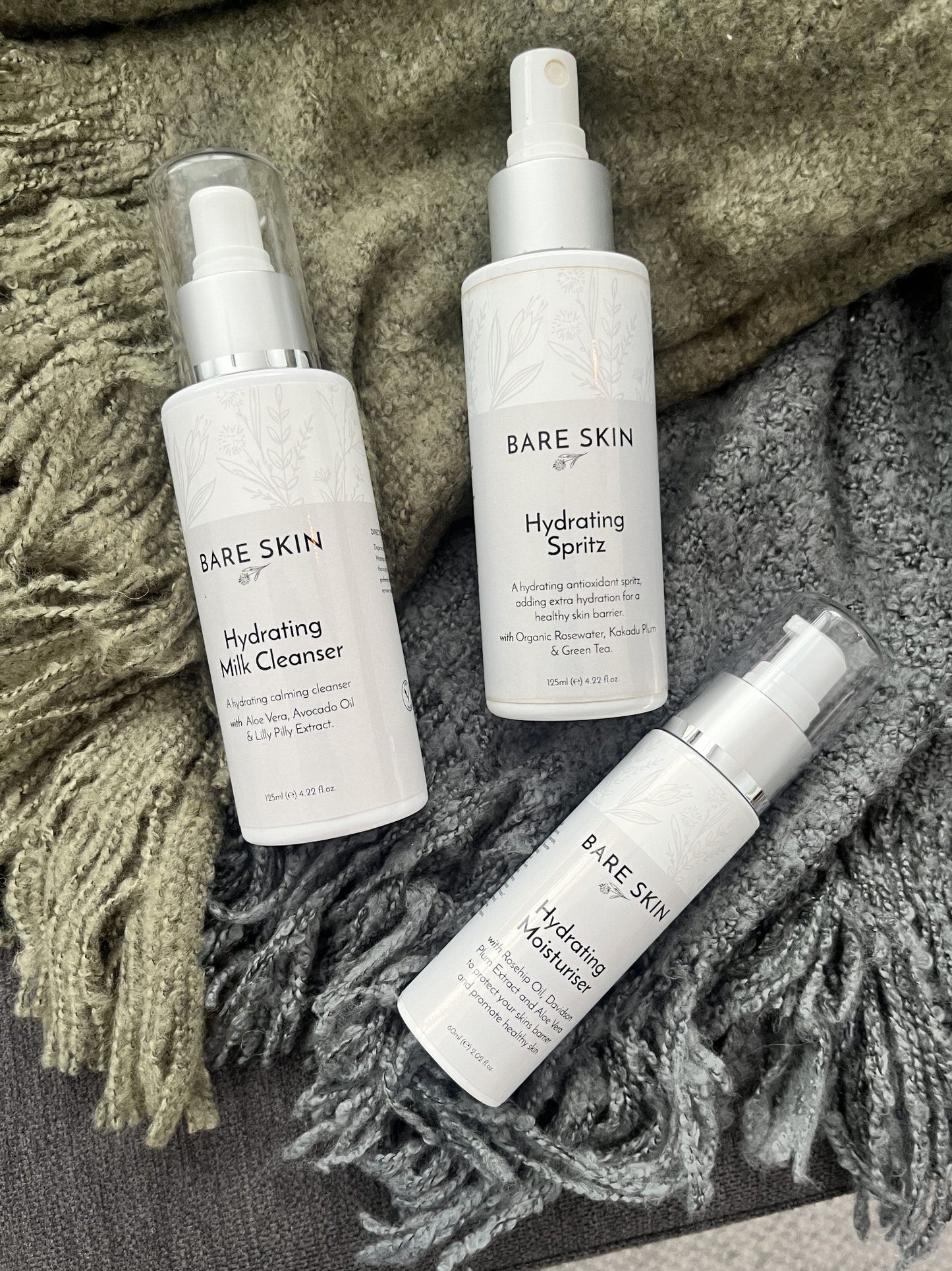 Three bottles of Bare Skin skincare products on a textured fabric background