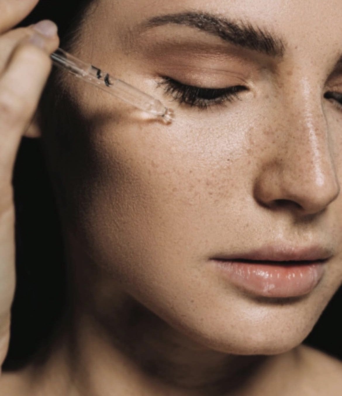 Close-up of woman applying Bare Skin Vitamin C Booster brightening antioxidant serum with Kakadu Plum using dropper to skin.