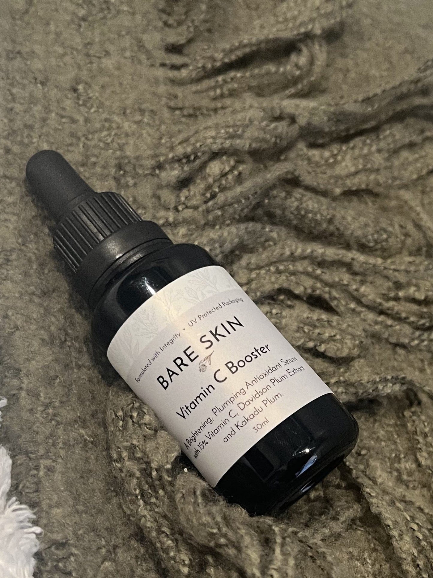 Bare Skin Vitamin C Booster brightening antioxidant serum with Kakadu Plum bottle on green blanket, skincare for radiant glowing skin.