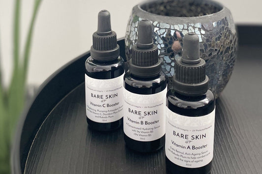 Bare Skin Vitamin A, B & C Booster Serums sitting on a black table with a vase and plant in the background