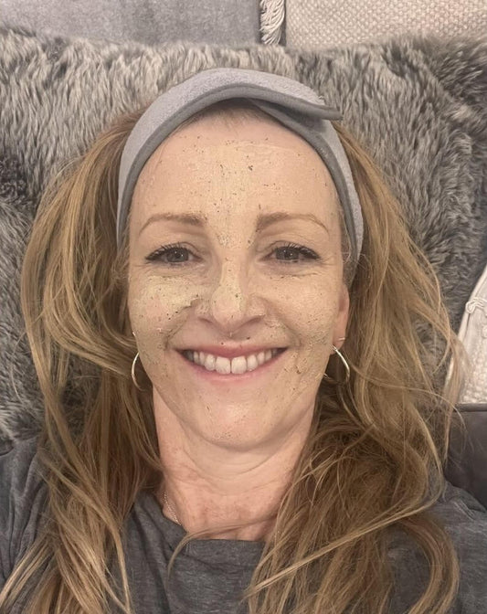 Woman laying down on a grey cushion with a grey headband on, smiling and wearing the Bare Skin Nourishing Polish.