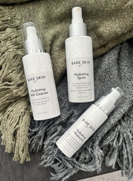 Three bottles of Bare Skin skincare products on a textured fabric 