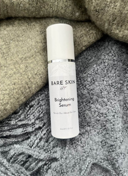 Bare Skin Brightening Serum bottle resting on a green and grey blanket, skincare for radiant glowing skin.