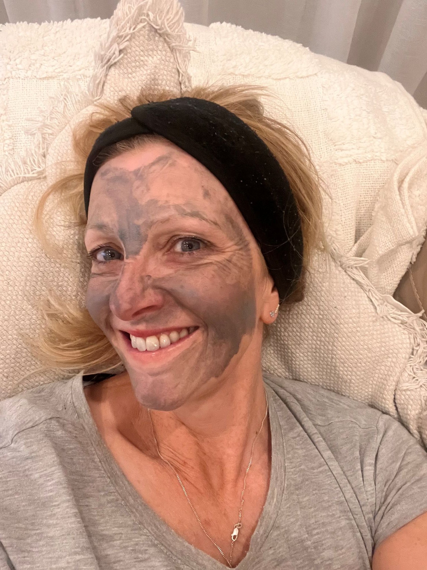 Lady wearing the Bare Skin Detox Charcoal Mask in a grey t-shirt laying on a white cushion