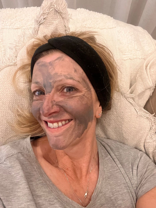 Lady wearing the Bare Skin Detox Charcoal Mask in a grey t-shirt laying on a white cushion