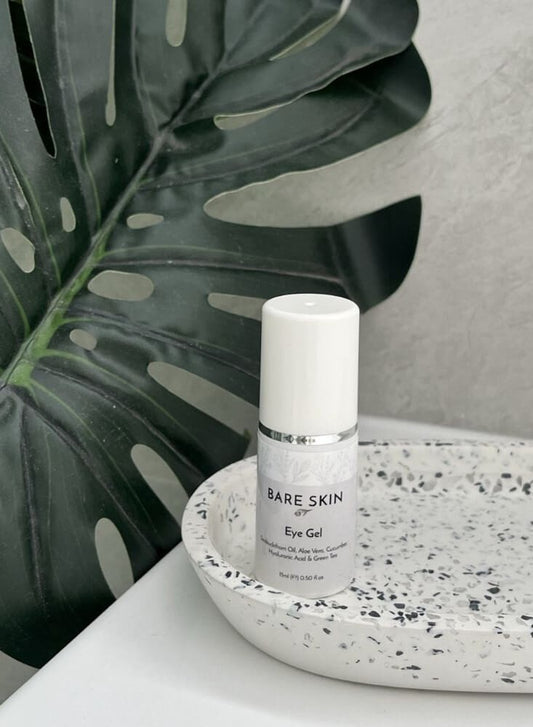 Bare Skin Cooling Eye Gel with Aloe Vera, Cucumber and Green Tea bottle on speckled ceramic tray with leafy background, soothing hydrating eye care.