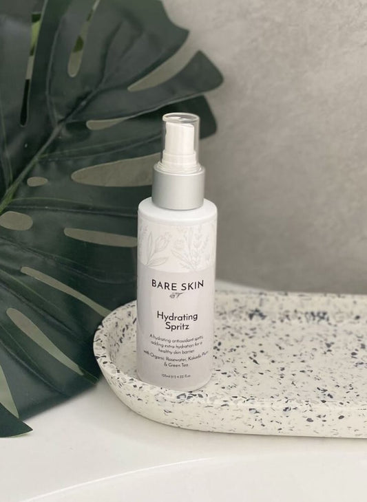 Bare Skin Hydrating Spritz bottle on a speckled surface with a leaf in the background