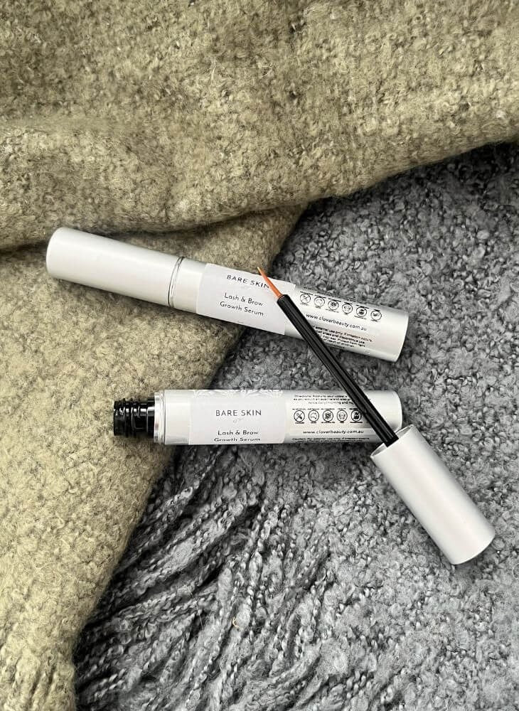Two Bare Skin Lash & Brow Serum placed on a textured fabric background, one closed and one open with the applicator wand resting across it.