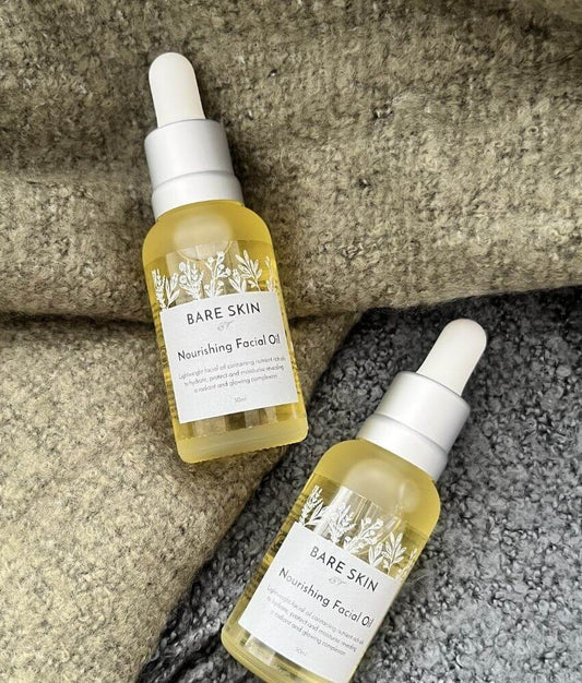 Two bottles of Bare Skin Nourishing Facial Oil laying a on grey and green blanket.