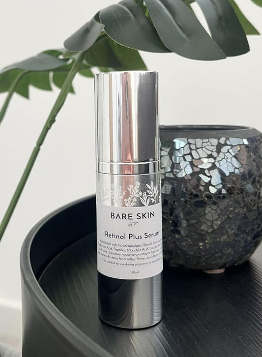 Bare Skin Retinol Plus Serum bottle on a dark surface with a plant in the background
