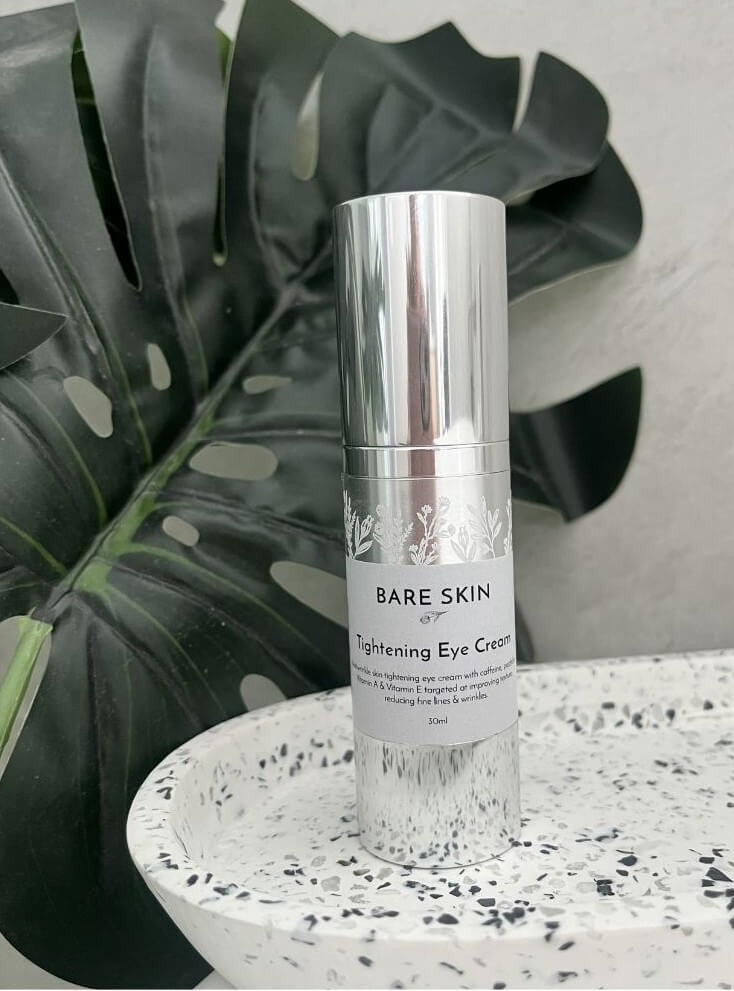 Bare Skin Tightening Eye Cream bottle on a speckled surface with a plant in the background